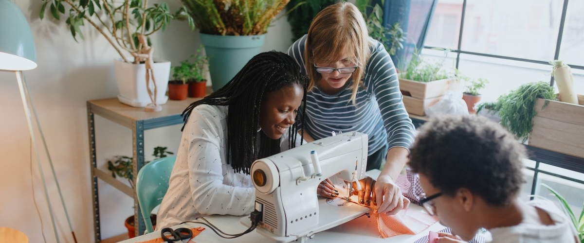 People gather around a sewing machine on a table